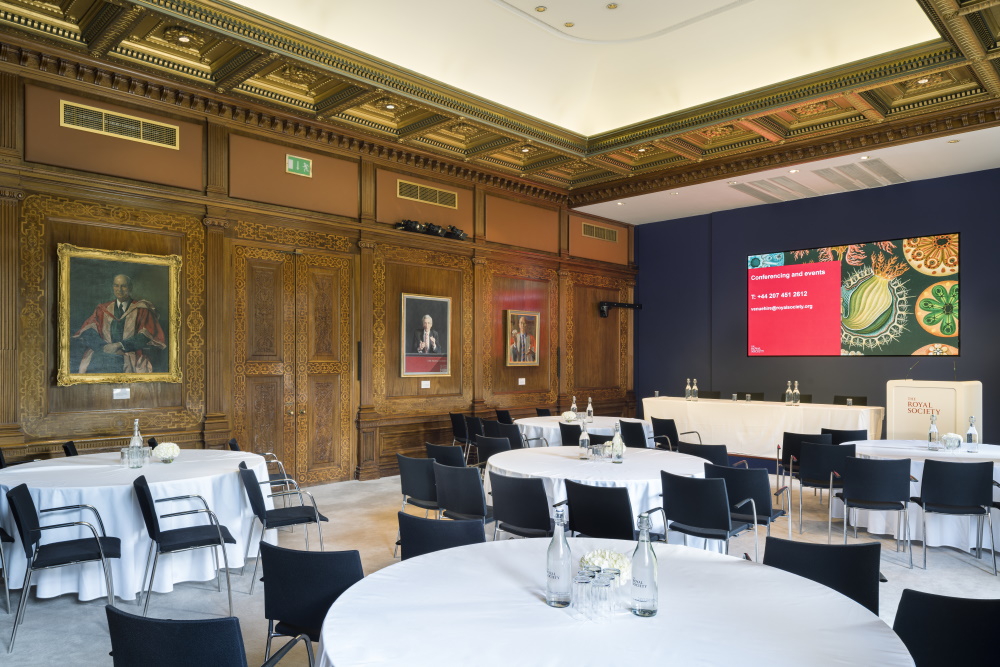 Five round tables with chairs facing towards a projector screen.