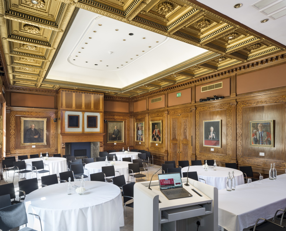 Five round tables with chairs facing towards a projector screen.