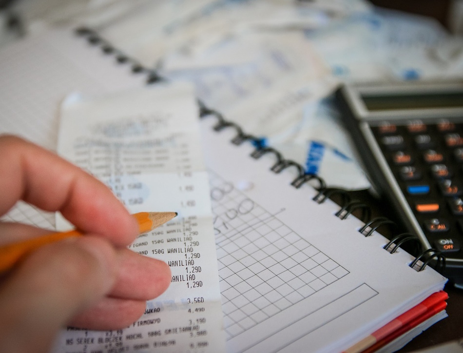 A hand holding a pencil next to a receipt and a calculator